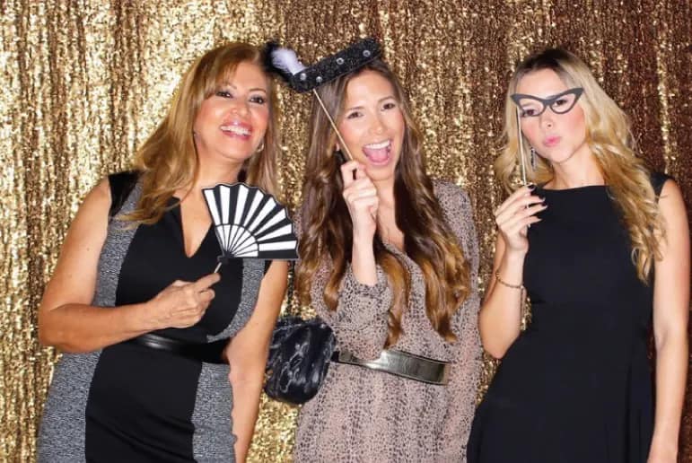 Three event guests posing with props against a gold sequin backdrop